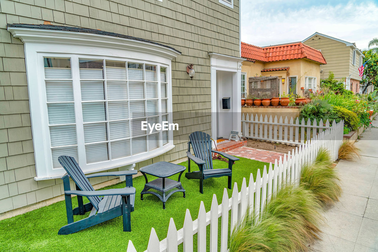 EMPTY CHAIRS OUTSIDE HOUSE IN YARD AGAINST BUILDINGS