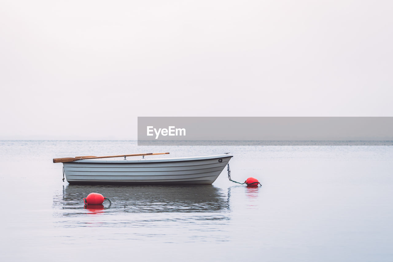 White boat with red buoys nearby in water against misty foggy sky