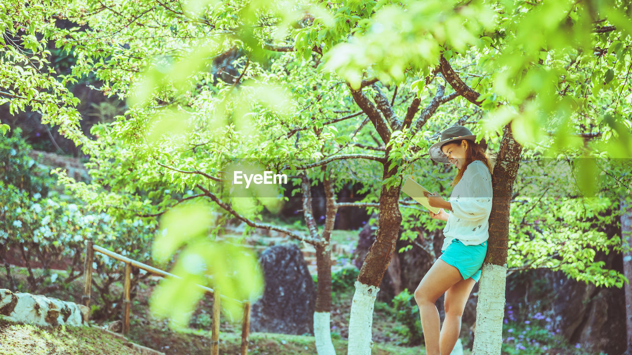 YOUNG WOMAN STANDING BY PLANTS