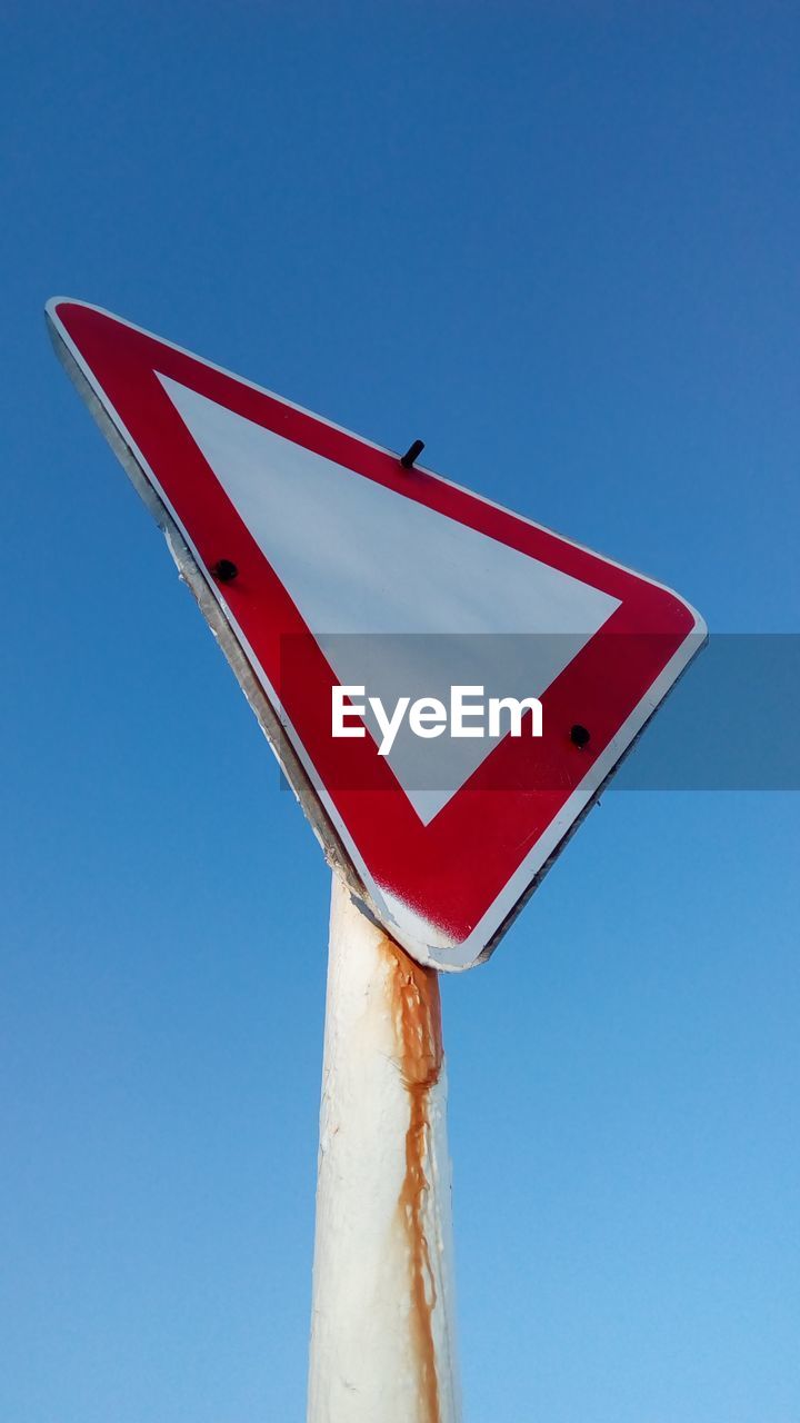 Low angle view of road sign against clear blue sky