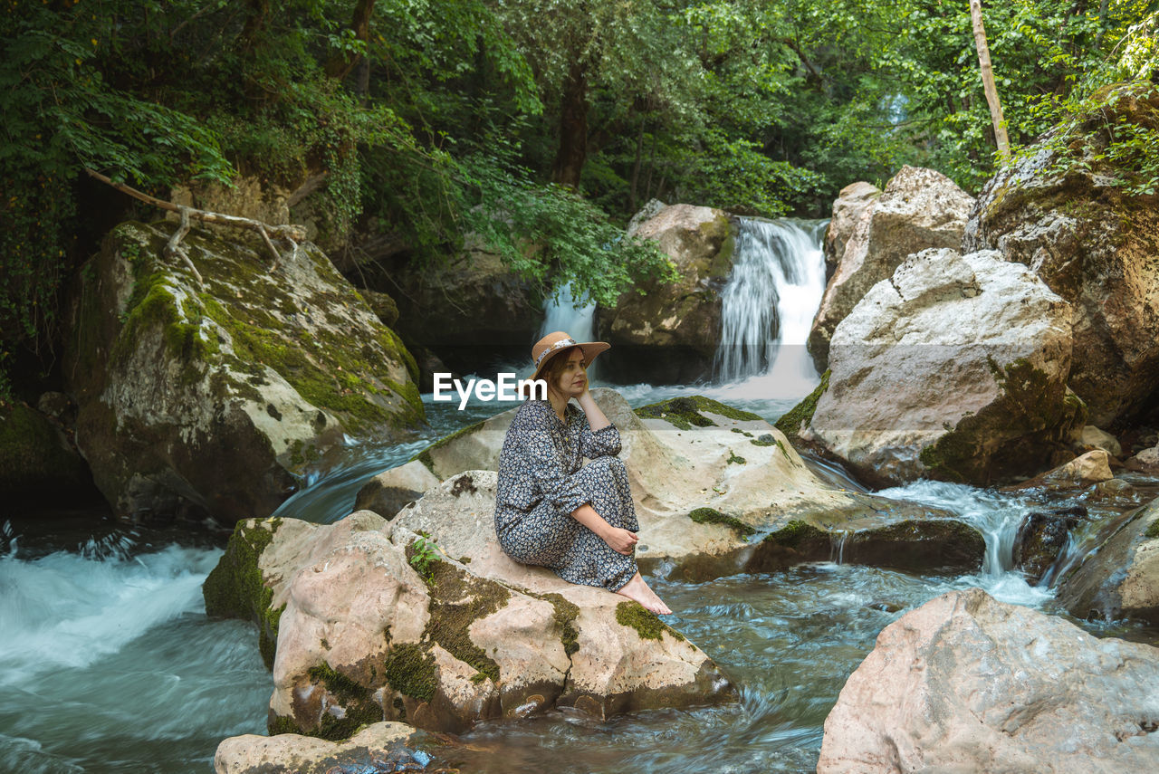 Young woman with hat enjoying in nature, relaxing and thinking in beautiful water oasis