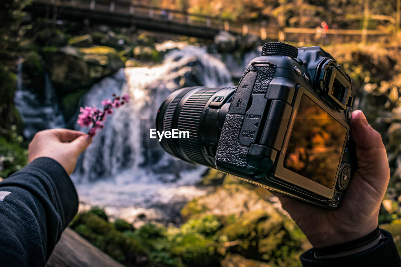 Cropped hand holding camera against waterfall