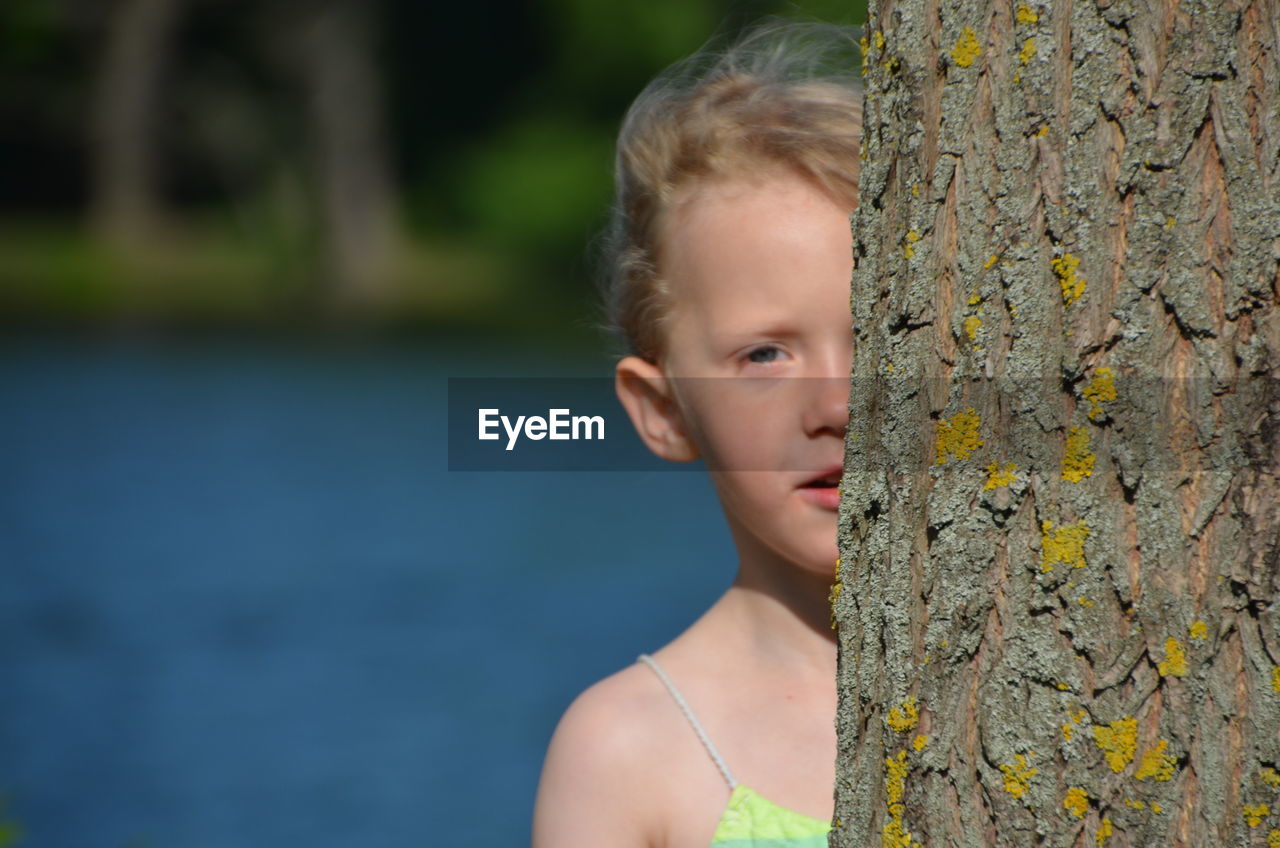 Portrait of cute girl by tree trunk against lake