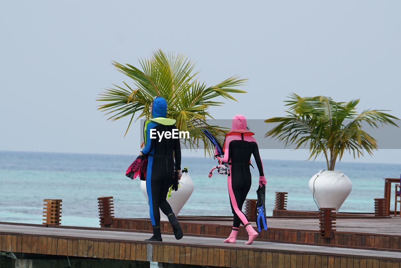 Full length of friends wearing diving suits while walking on pier