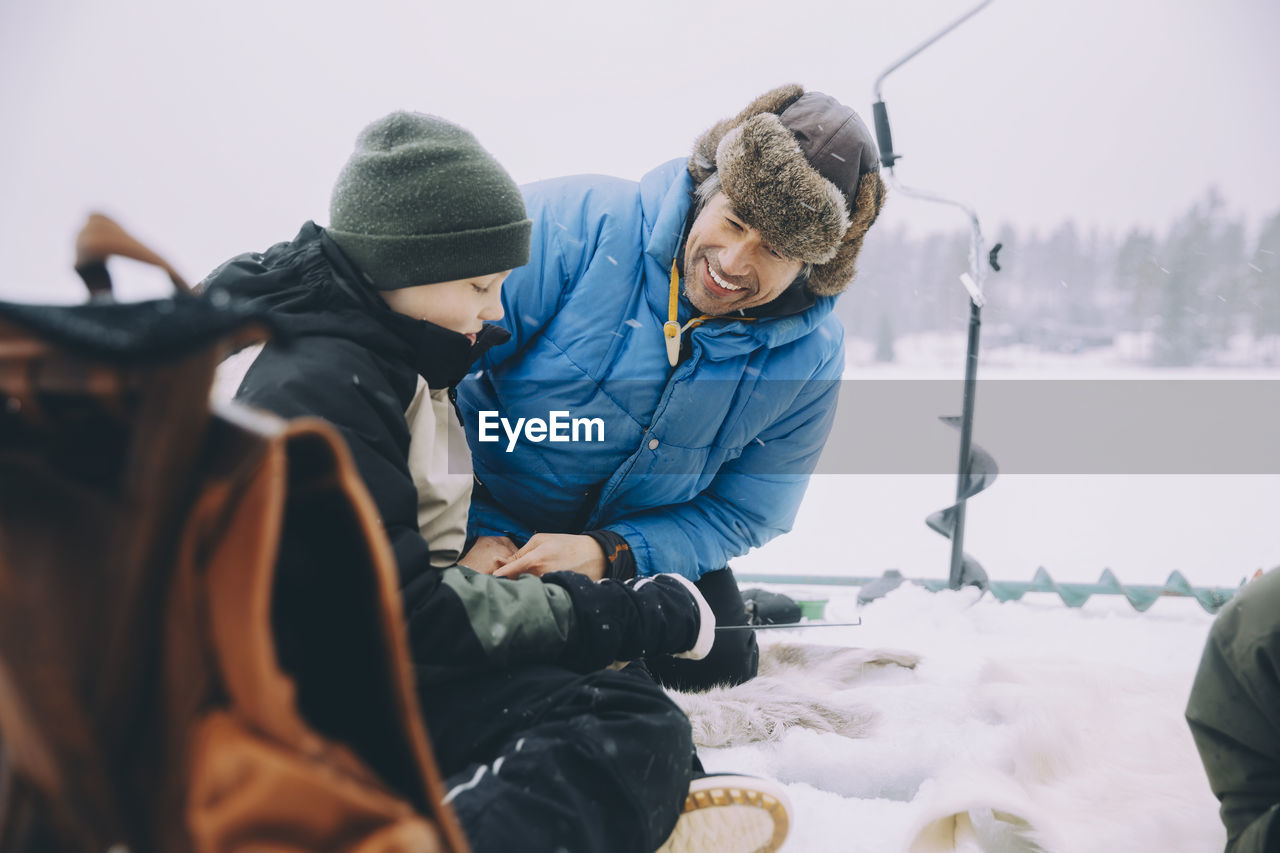 Happy father talking with son sitting on frozen lake