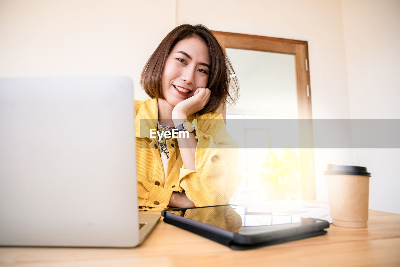 Young elegant businesswoman in yellow shirt and cup of coffee sitting with laptop in cafe. 