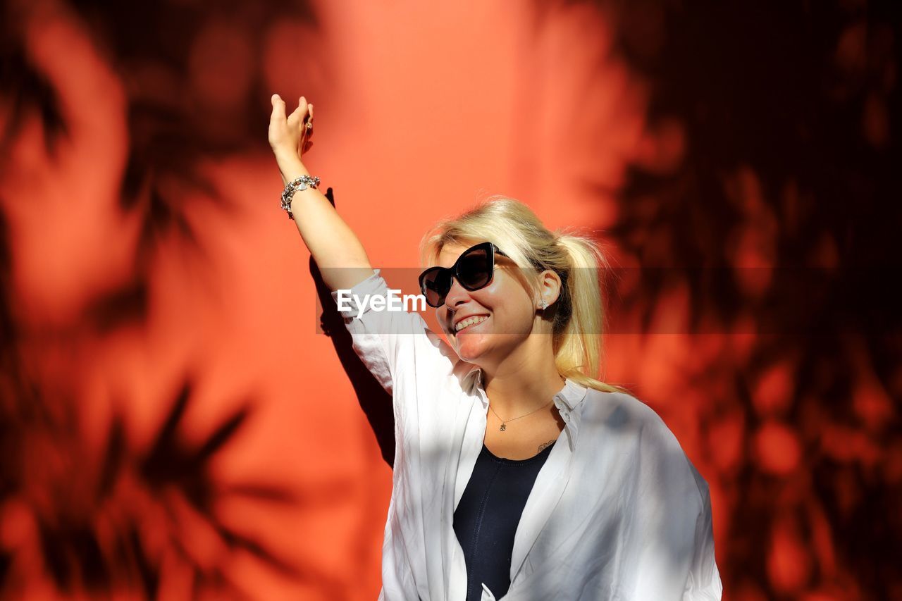 Happy woman wearing sunglasses while standing against wall