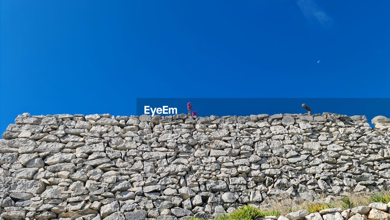 sky, blue, nature, architecture, clear sky, rock, stone wall, day, sea, built structure, wall, copy space, outdoors, travel, ruins, sunny, archaeological site, land, travel destinations, one person, history, men