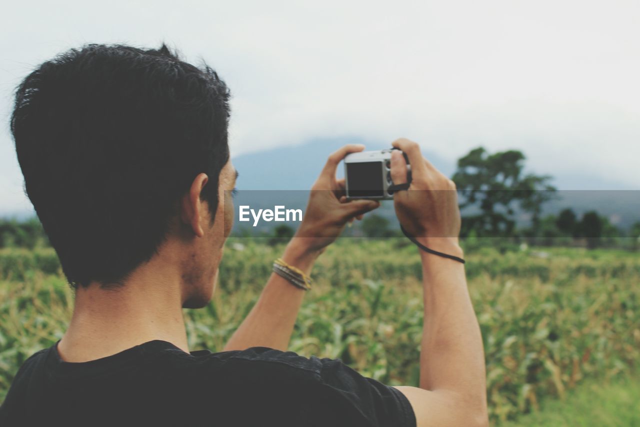 Rear view of man photographing through camera on field