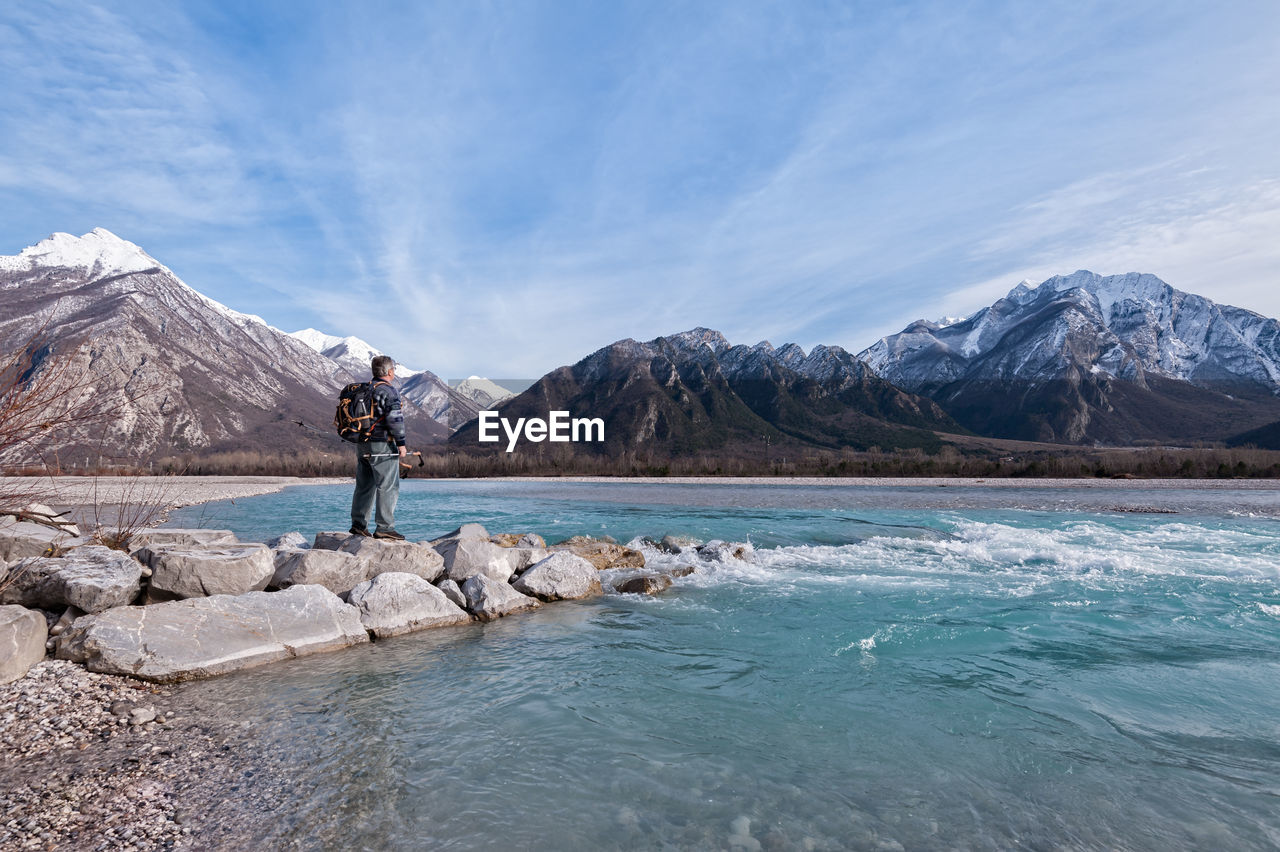 Hiker standing on rock by lake against sky