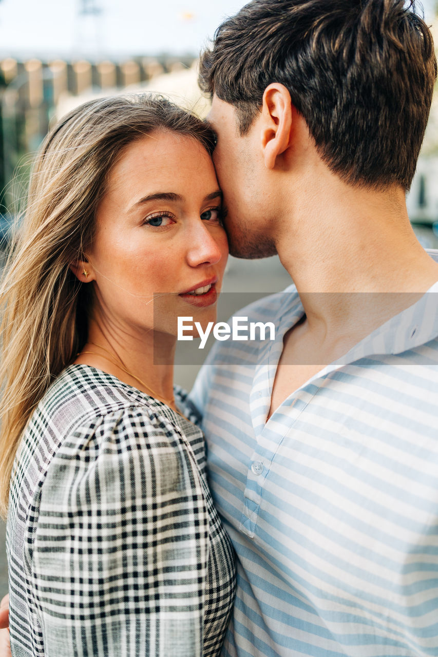 Smiling couple in trendy clothes standing in city street and embracing with love