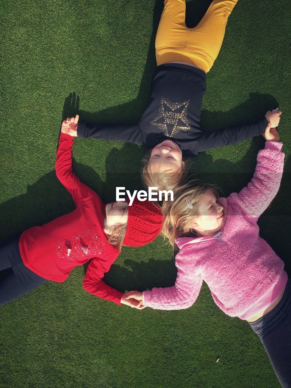 3 young girls hold hands whilst lying on the ground in a circle