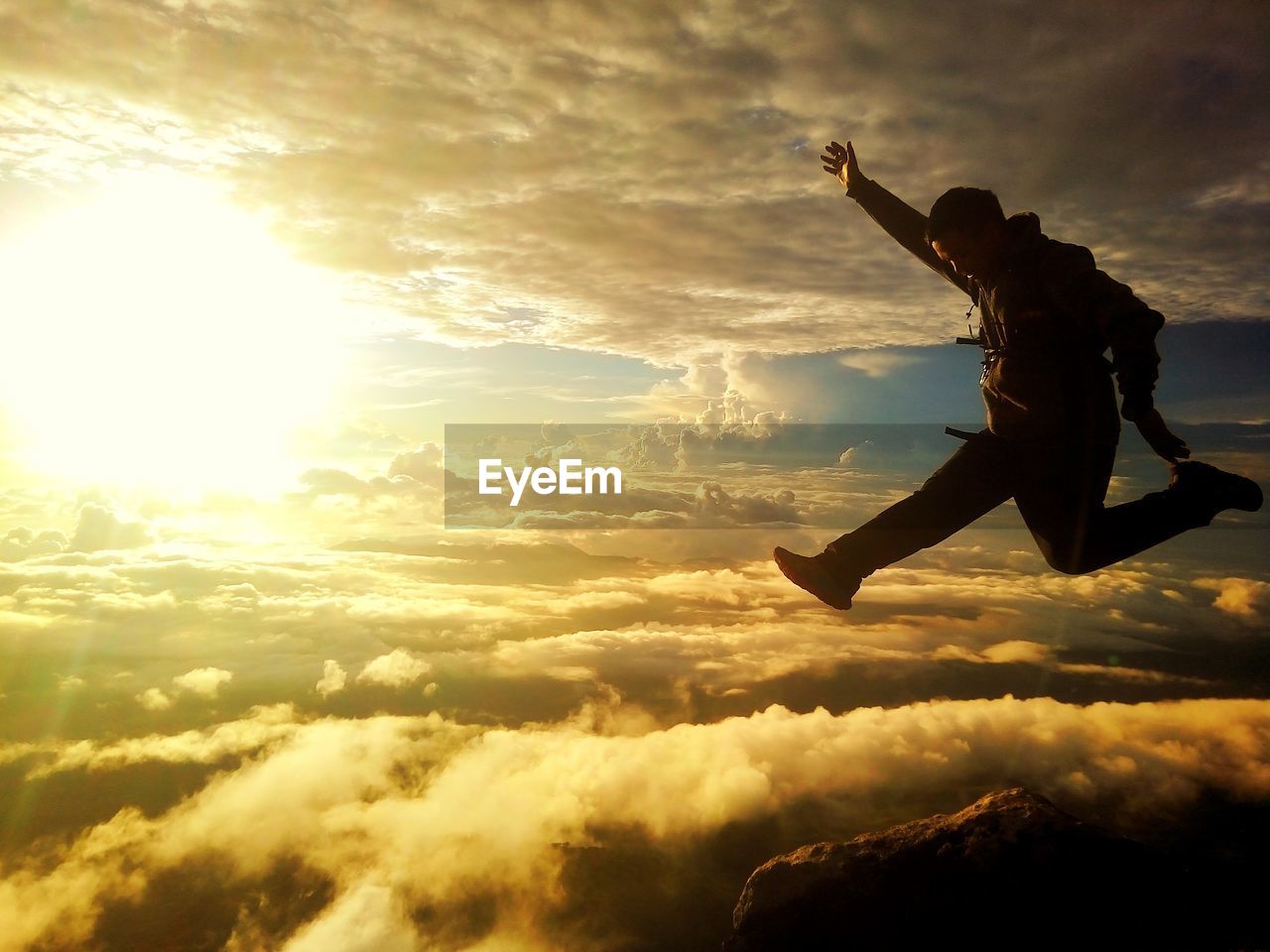 Man jumping over cloudscape against sky during sunset