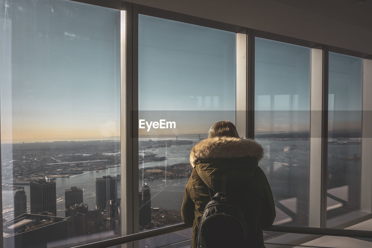 REAR VIEW OF WOMAN LOOKING THROUGH GLASS WINDOW