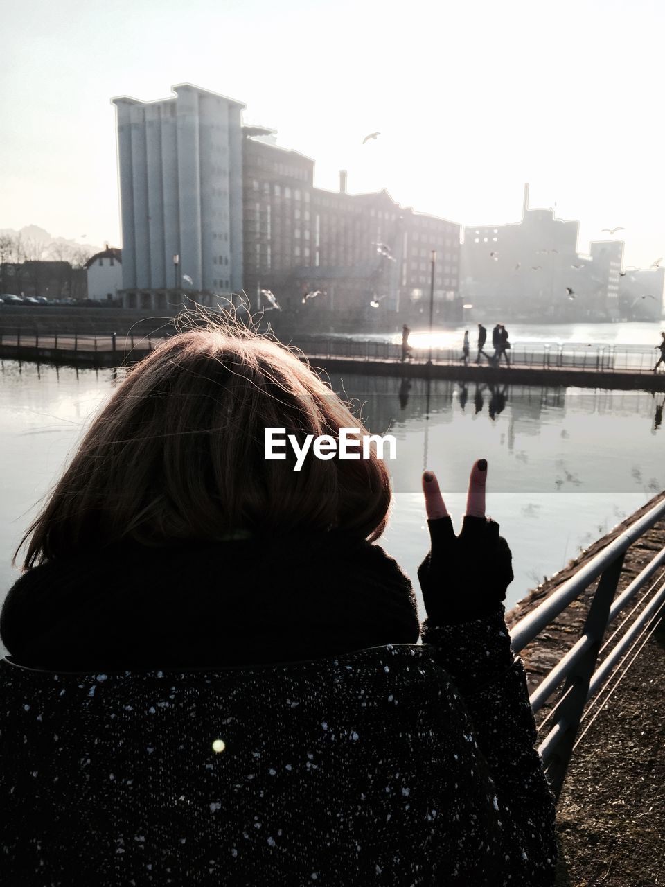 Rear view of woman showing peace sign at harbor