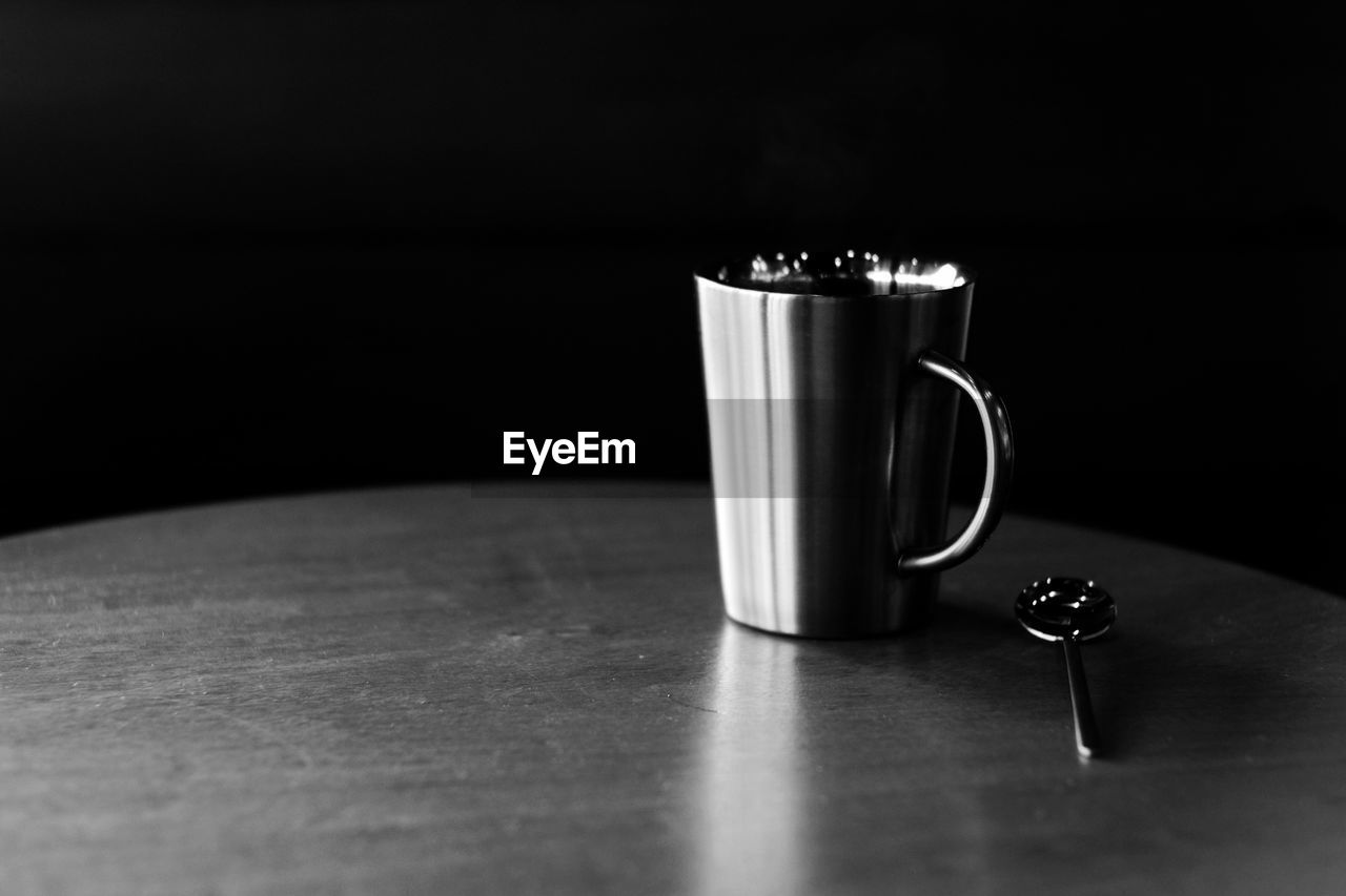 CLOSE-UP OF COFFEE CUP ON TABLE AGAINST BLACK BACKGROUND