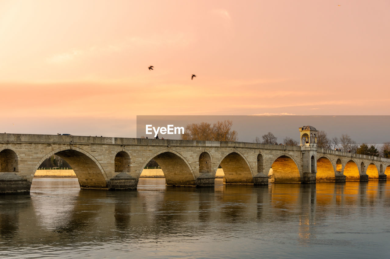 BRIDGE OVER RIVER AGAINST SKY AT SUNSET