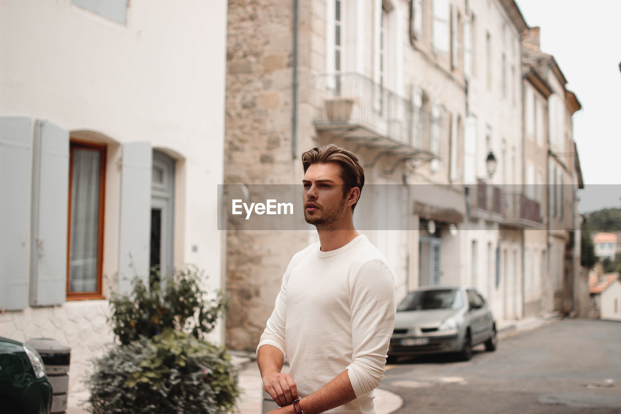 Young man looking away while standing on street in city