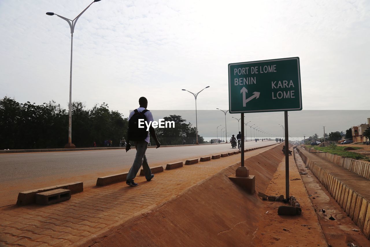 REAR VIEW OF MAN STANDING BY ROAD