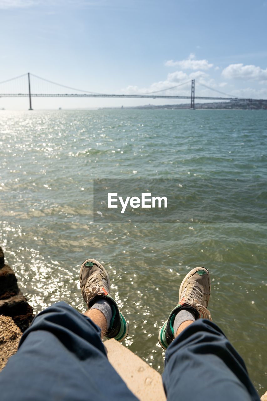 Low section of man sitting by sea against sky