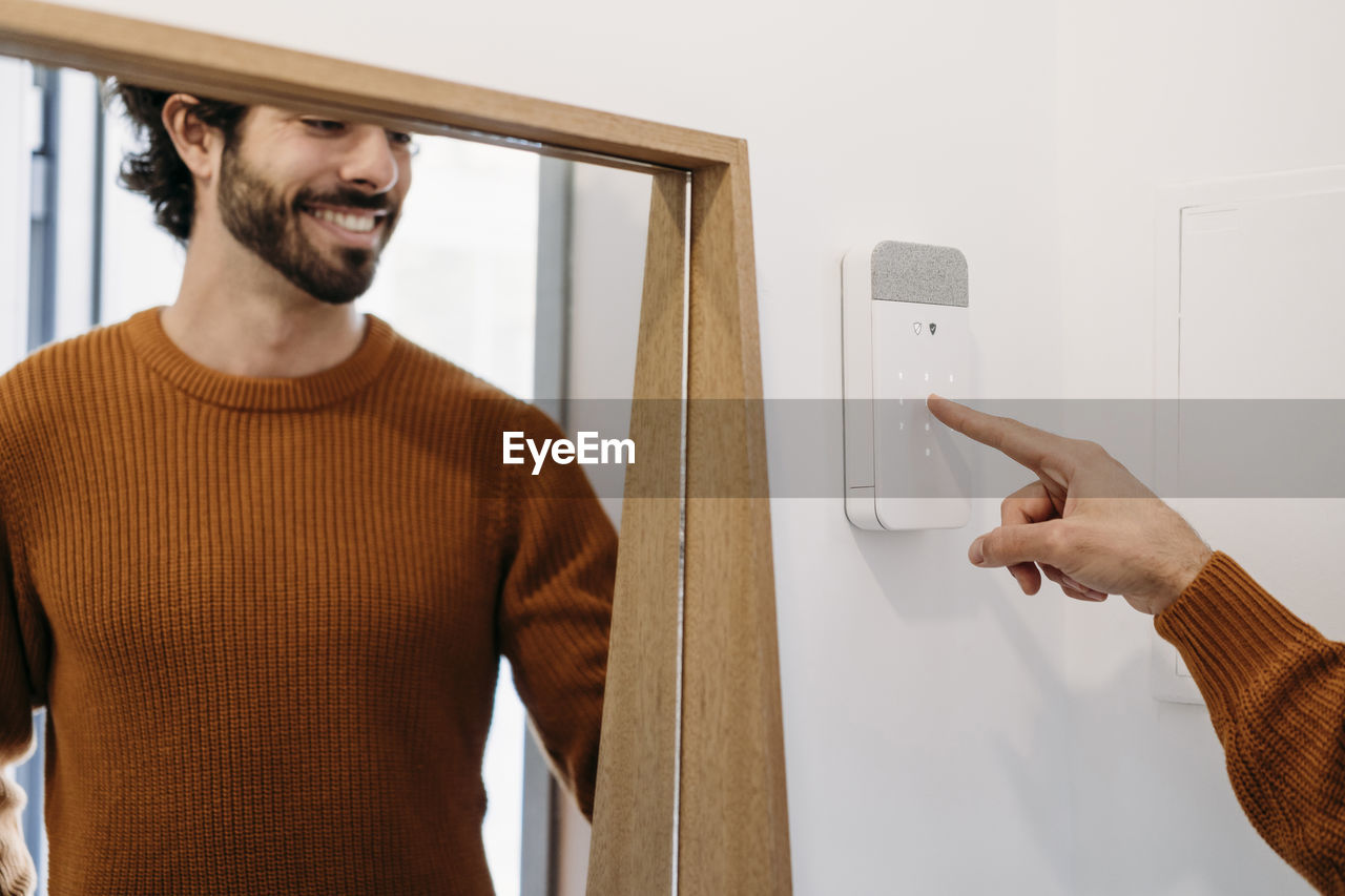 Happy young man setting alarm system at home