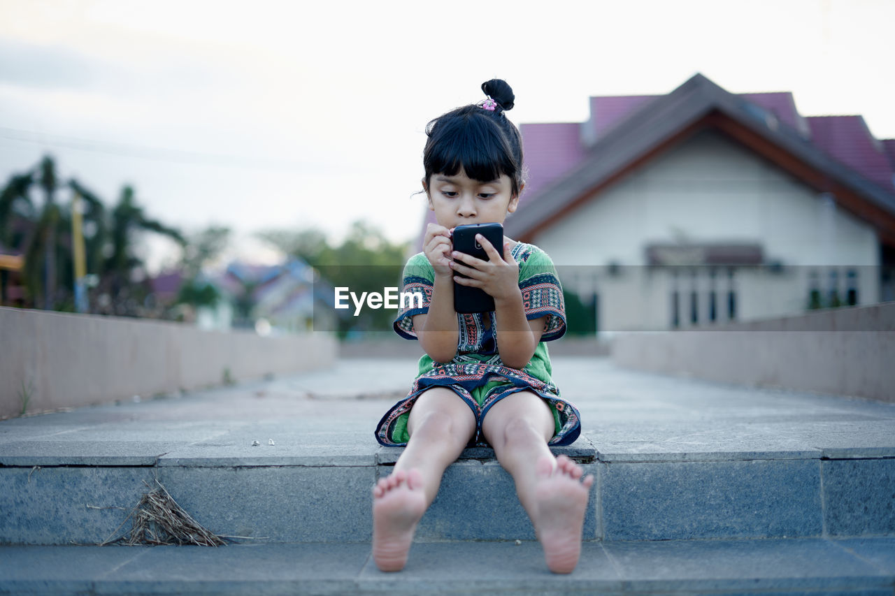 Full length of girl using phone against clear sky