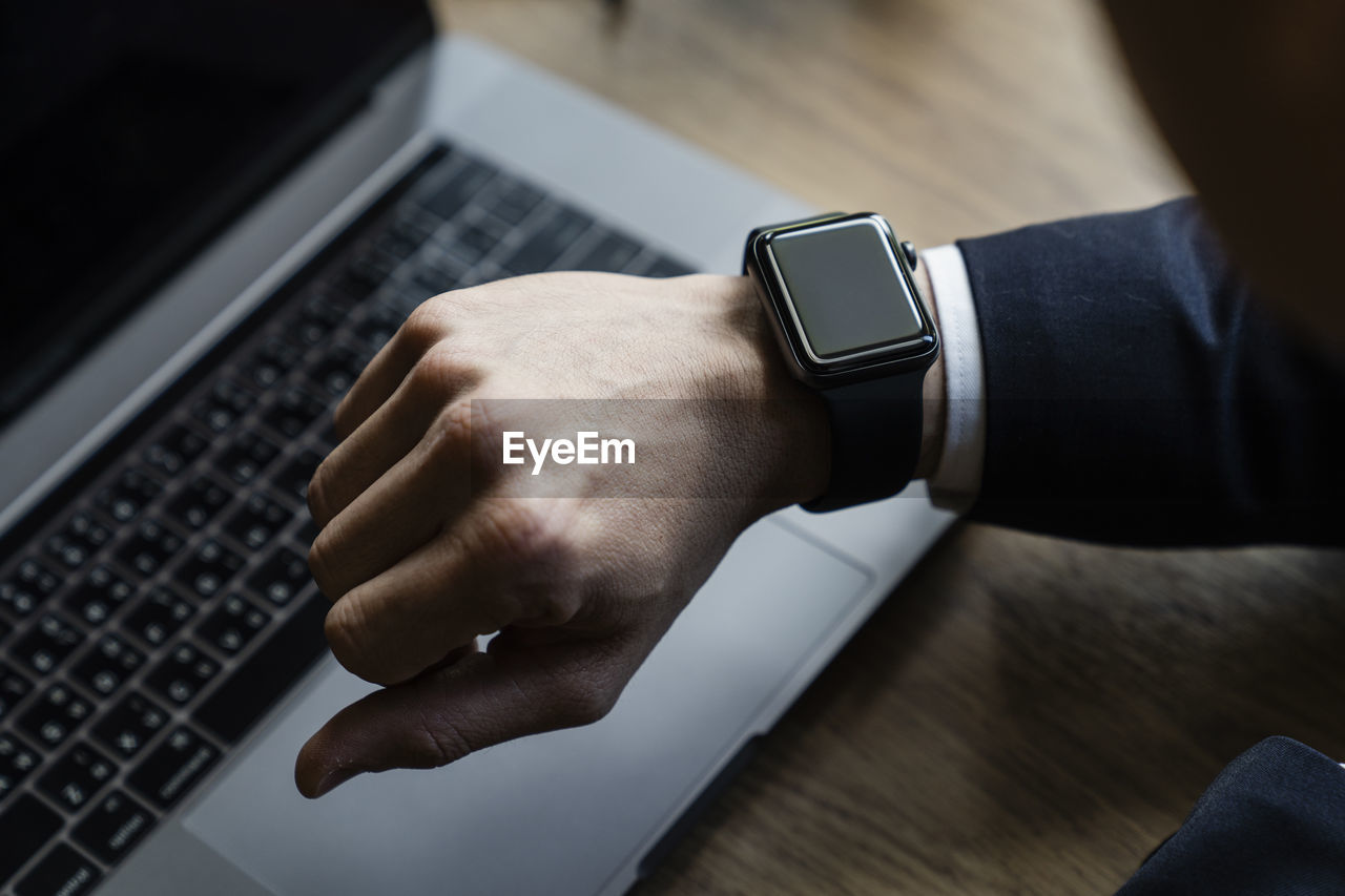 Cropped hand of man checking time against laptop