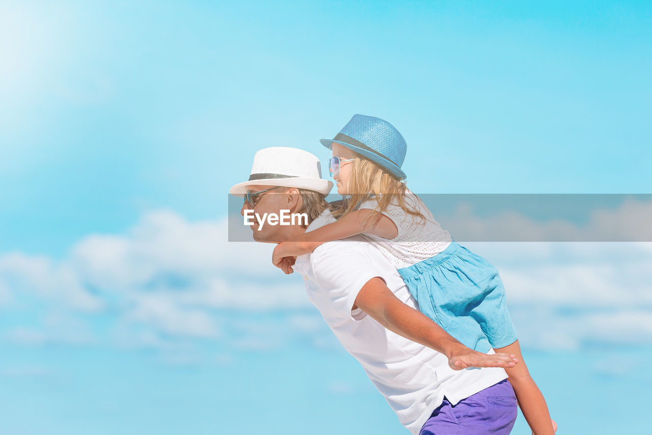 Side view of father carrying daughter against sky