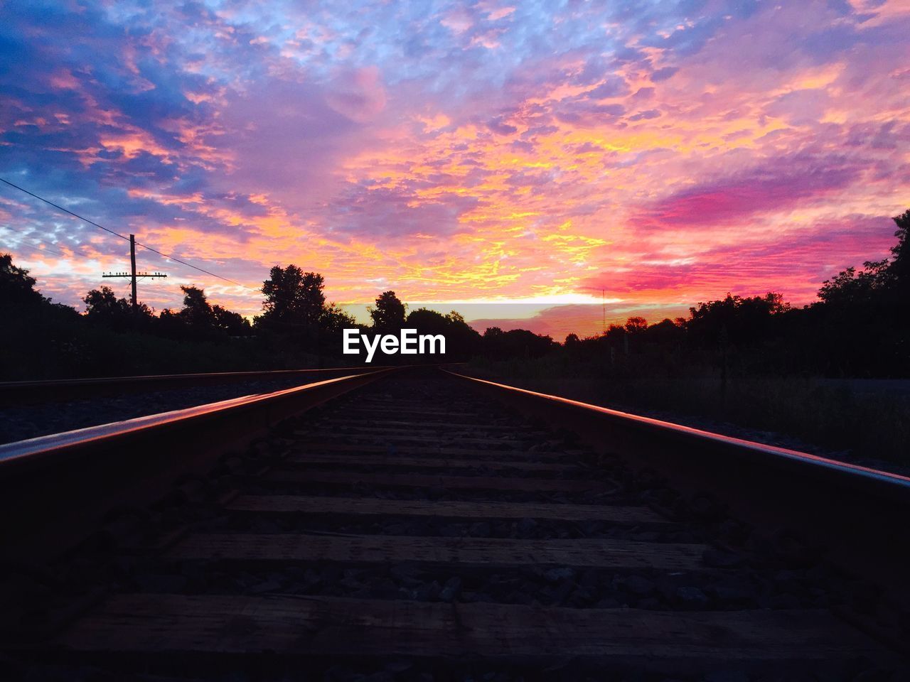 Railroad track against cloudy sky during sunset