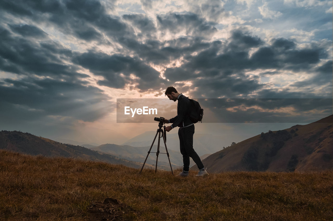 Man photographing at camera against sky during sunset