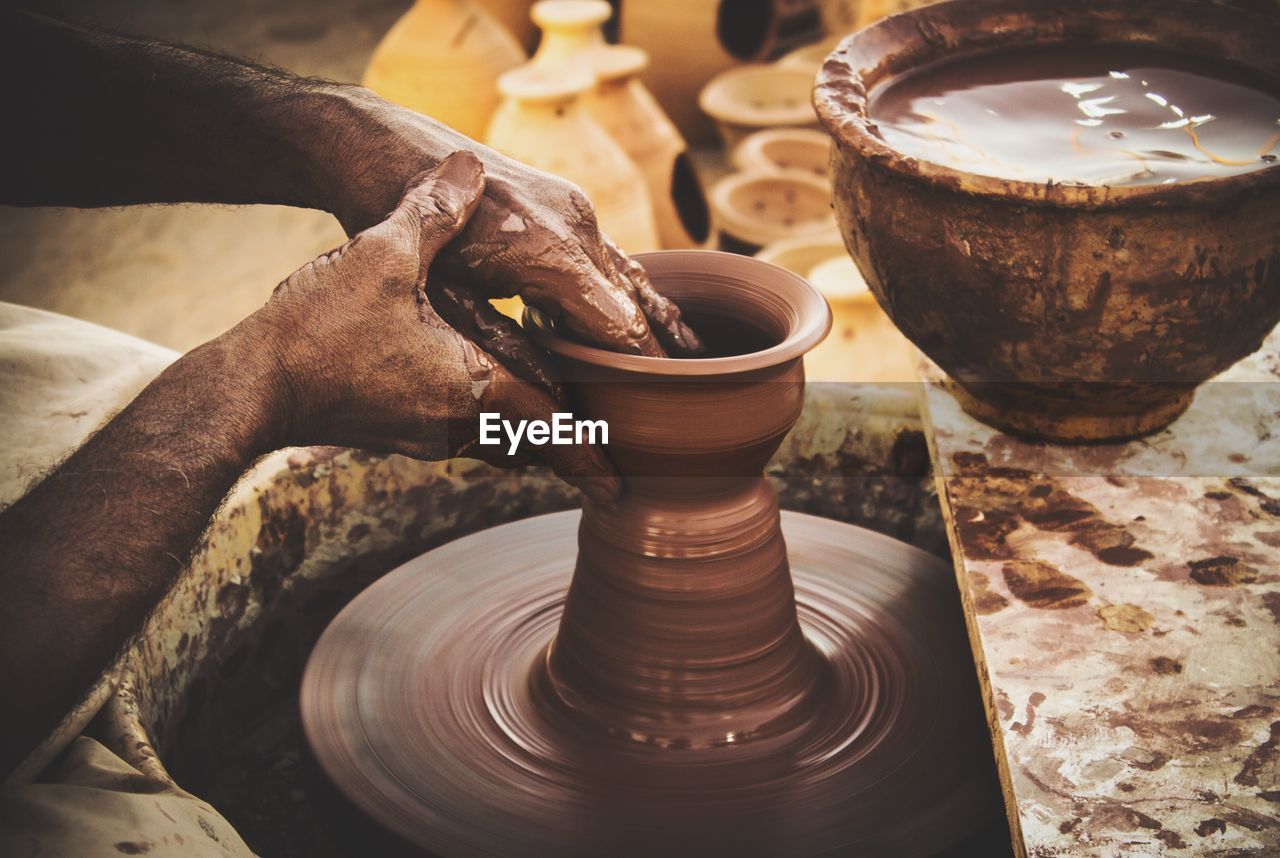 Cropped image of hands making earthen pots on wheel at workshop