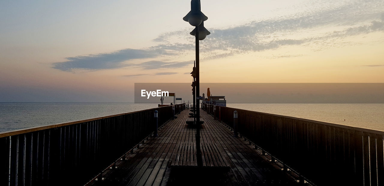 Street light on pier by sea against sky during sunset