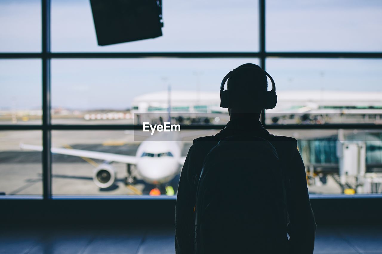 Rear view of man listening music while looking through window in airport