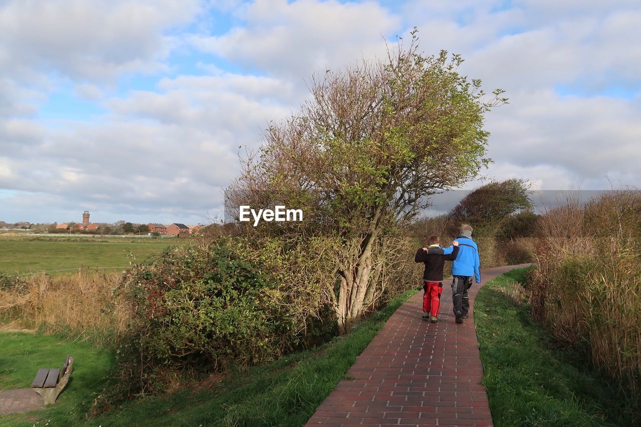 REAR VIEW OF PEOPLE WALKING ON ROAD AMIDST FIELD