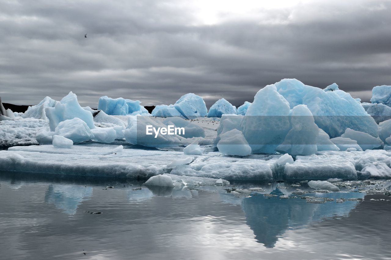 Scenic view of glaciers melting against cloudy sky