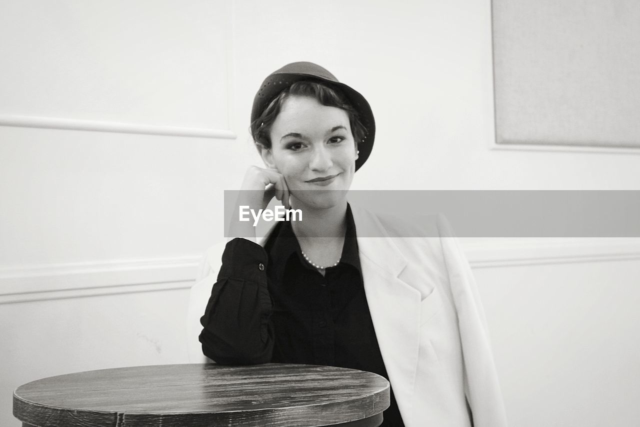 Portrait of smiling young woman sitting against wall