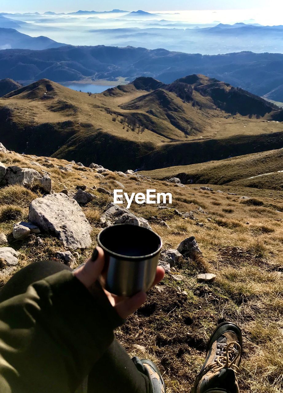 Cropped hand of woman holding coffee cup against landscape