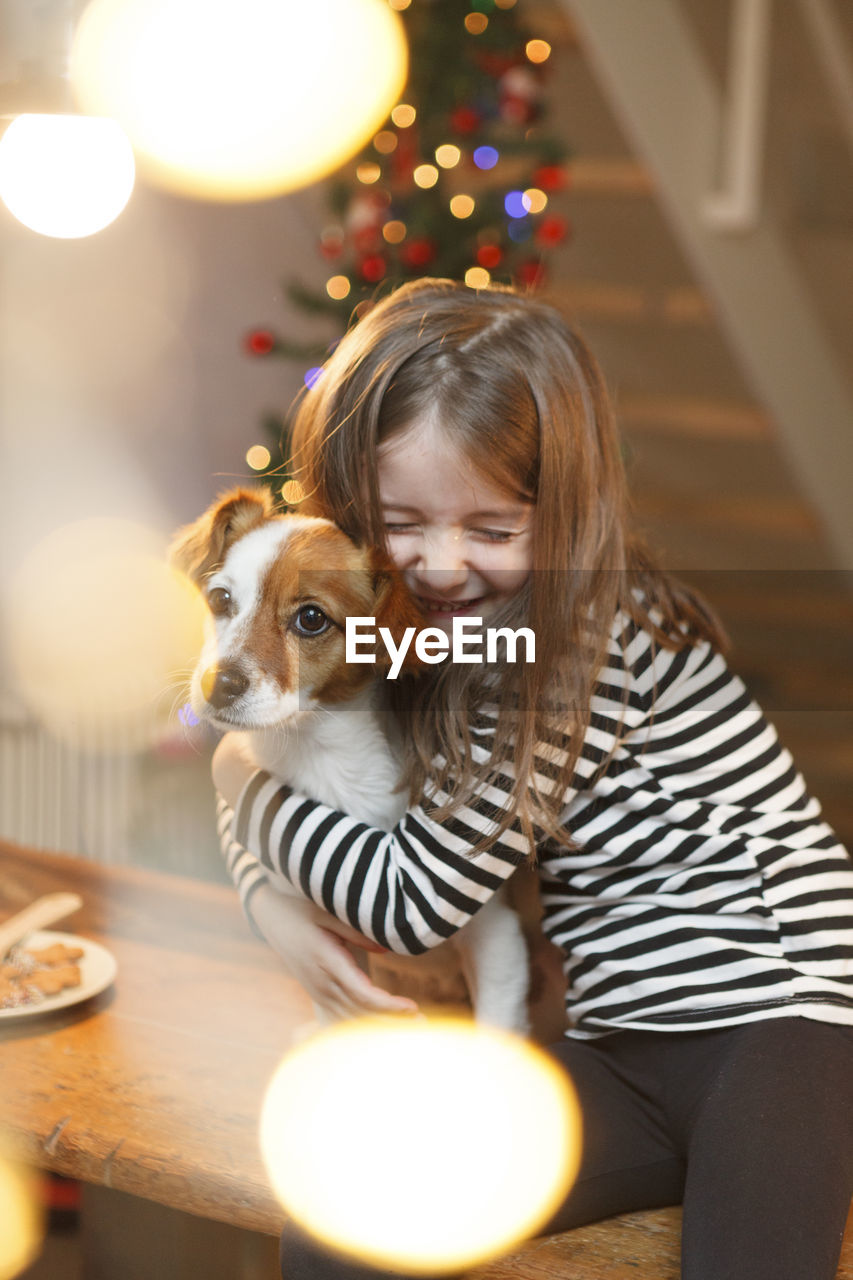 Smiling girl embracing while sitting at home during christmas