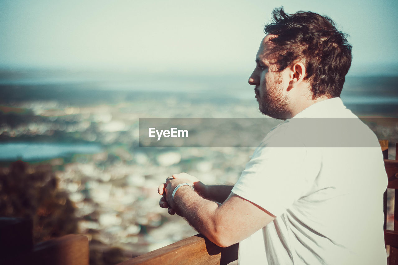 Side view of thoughtful young man standing by railing