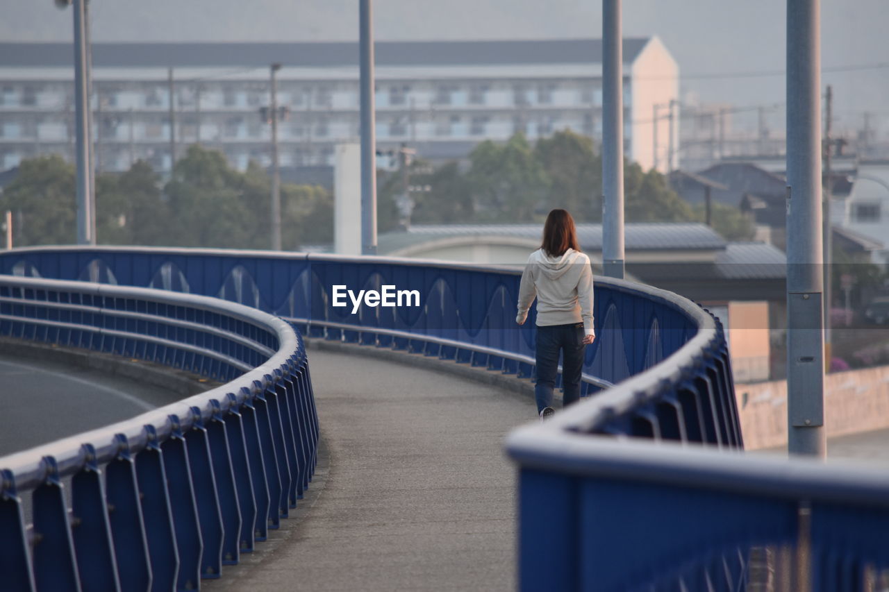 Rear view of woman walking on bridge against building