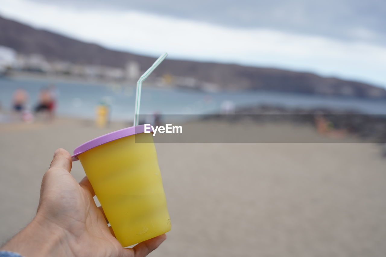 Holding plastic cup with drinking straw at beach