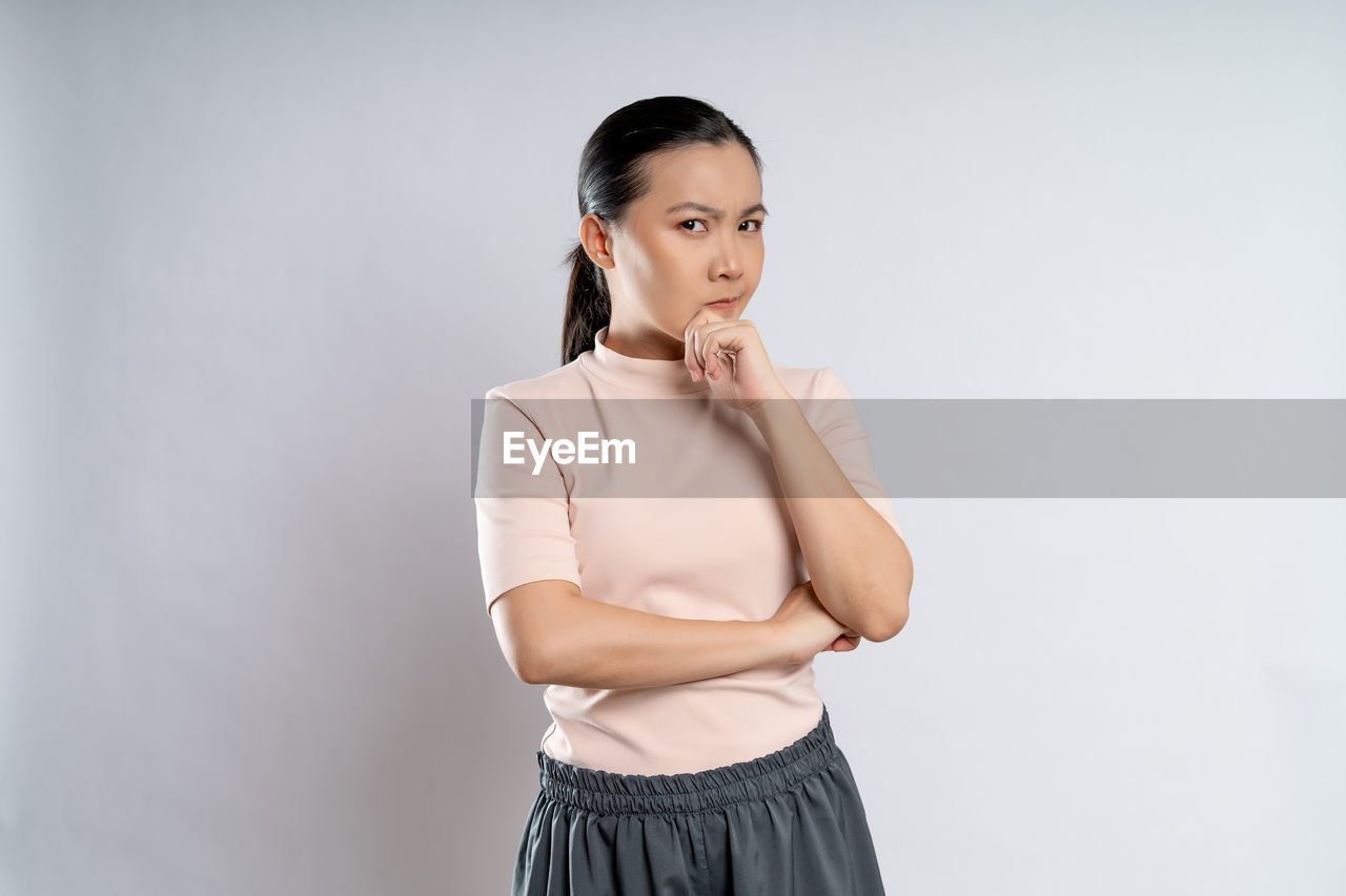 one person, women, studio shot, adult, sleeve, indoors, portrait, photo shoot, clothing, young adult, skirt, standing, gray background, gray, female, copy space, looking at camera, trunk, arms crossed, looking, emotion, collar, fashion, front view, waist up, serious, hairstyle, blouse, lifestyles, white background, arm, businesswoman, textile, smiling, person, outerwear, hand, human face