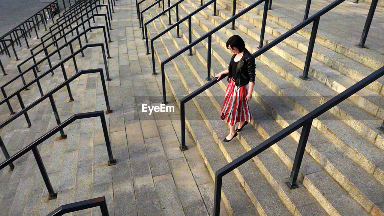 Full length of woman wearing striped skirt and jacket on steps amidst railing in city