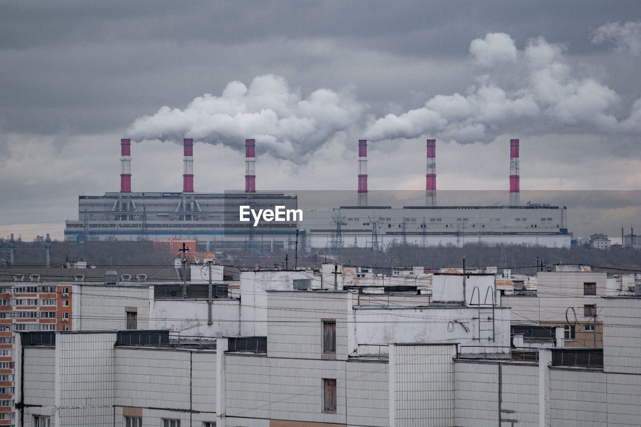 Smoke emitting from factory against cloudy sky