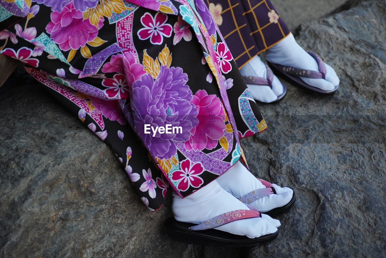 Surface level of women in traditional clothing floral dress sitting on rock