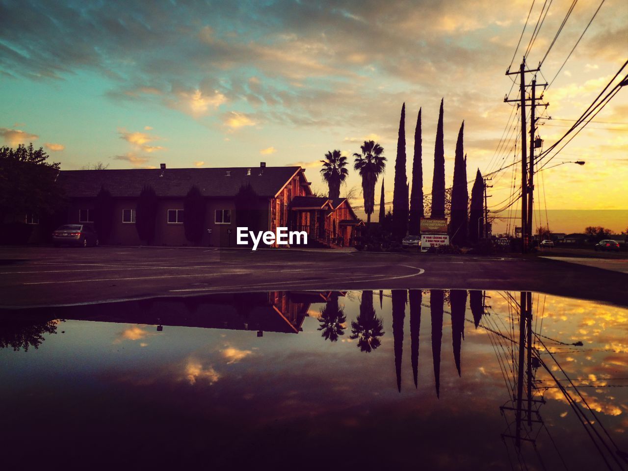 Reflection of trees and house in pond during sunset
