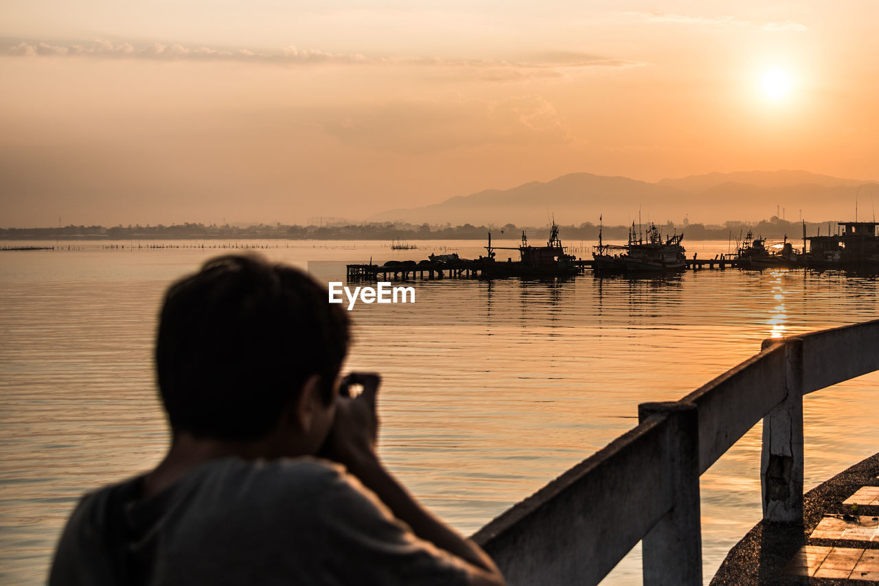 Rear view of man photographing by sea gainst sky during sunset