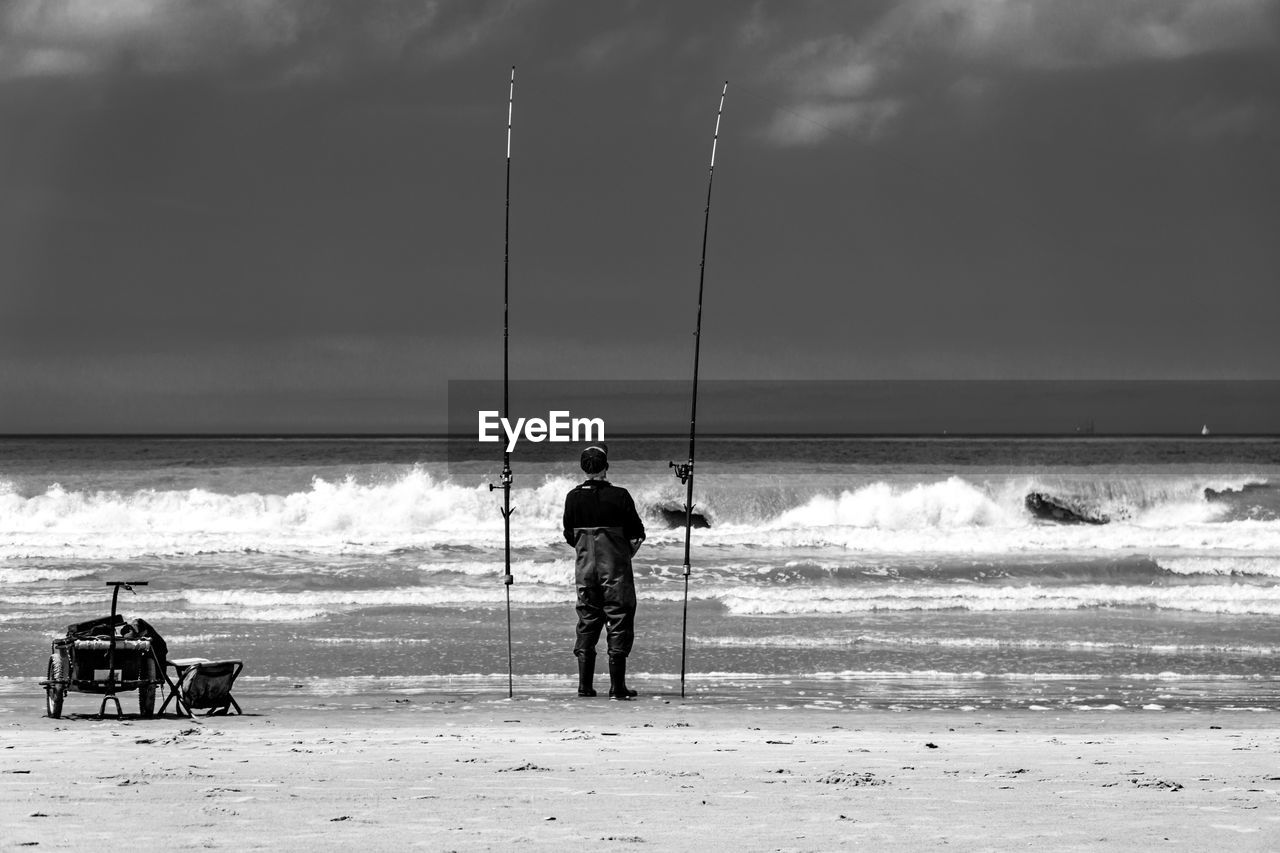 REAR VIEW OF PEOPLE STANDING ON BEACH