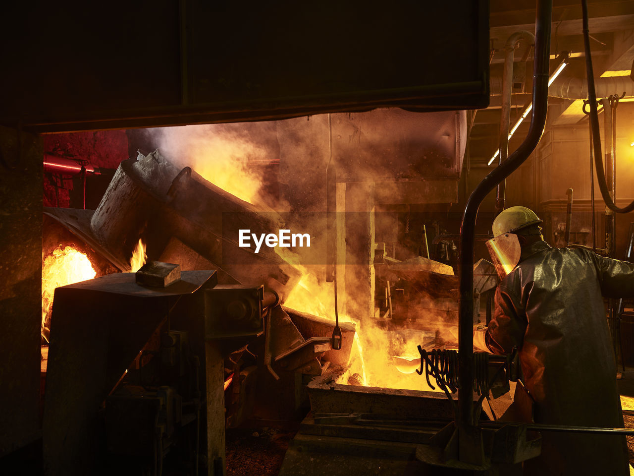 Rear view of worker working by furnace in foundry