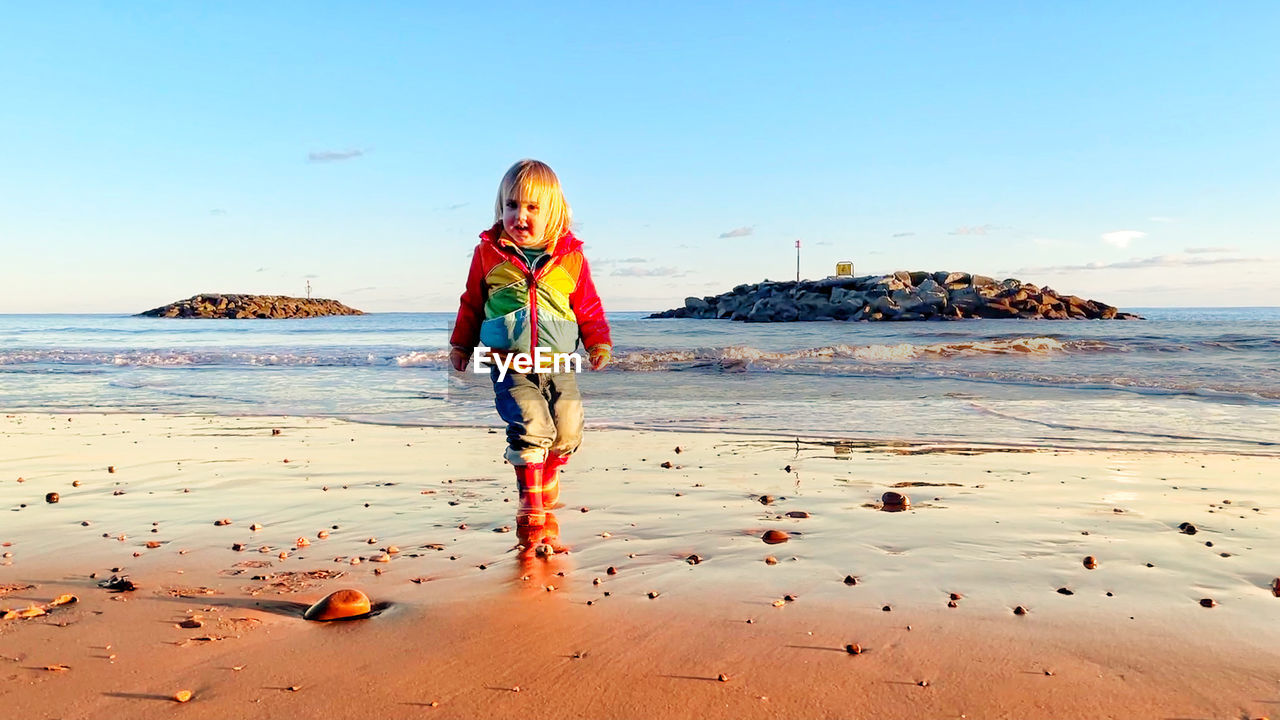 FULL LENGTH OF BOY STANDING ON BEACH AGAINST SEA